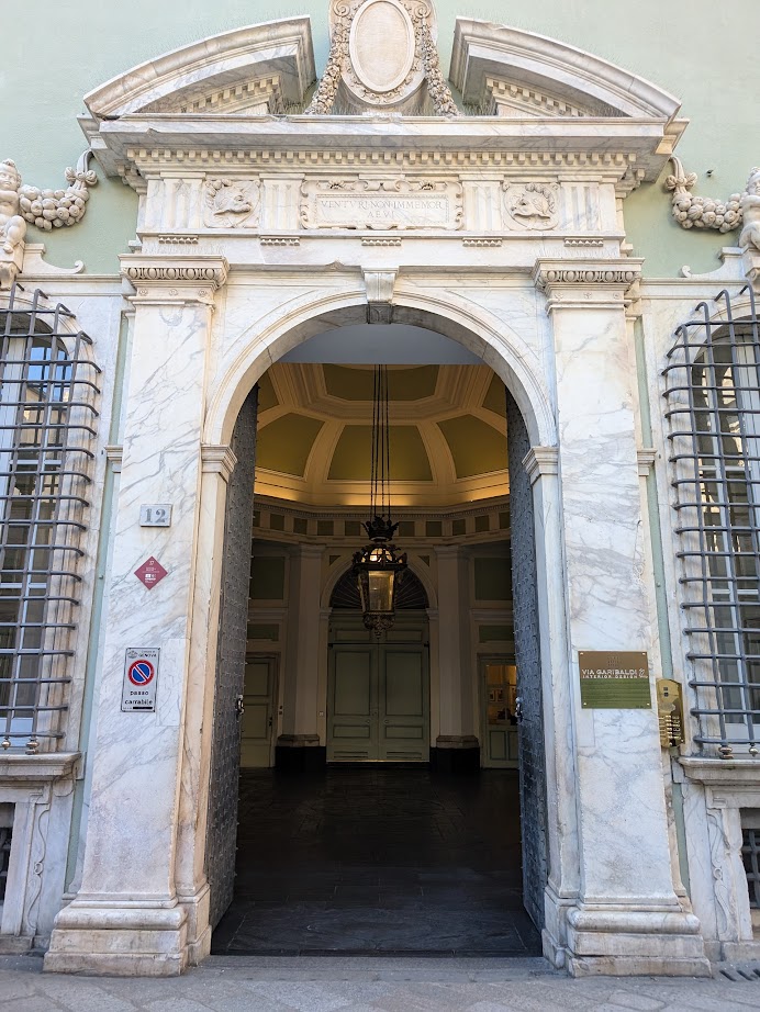 Ornate arched marble doorway with a hanging lantern, reminiscent of Genoa, Italy, leading into an elegant building interior—inviting exploration at any hour, even within 24 hours.