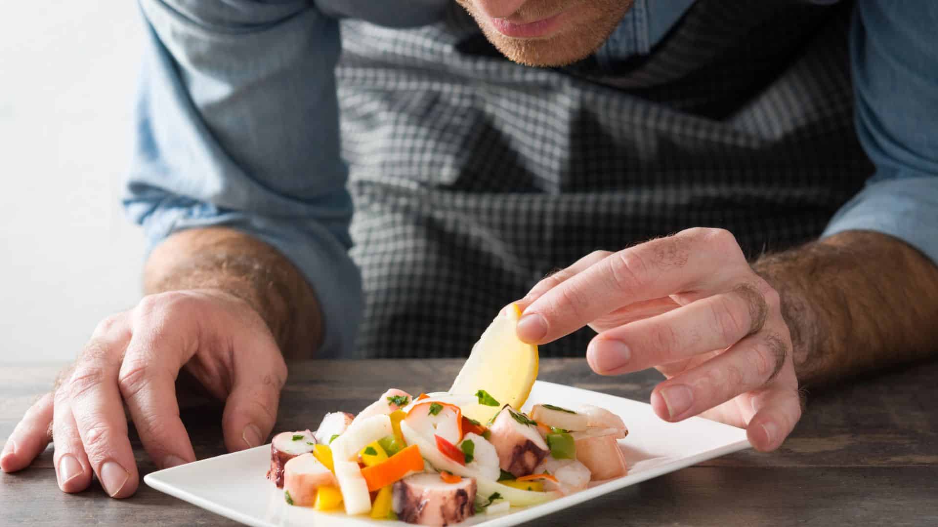 A chef carefully garnishes a plate of seafood and vegetables with a slice of lemon.