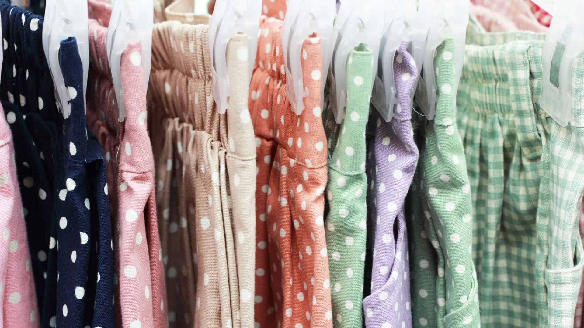 Colorful polka dot and checkered pants hanging on white plastic hangers in a row.
