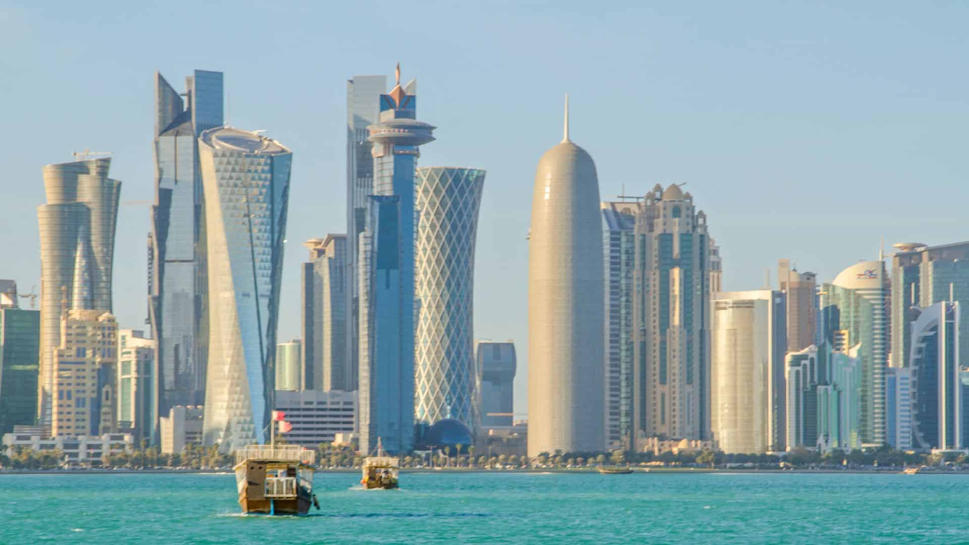 Boats on turquoise water with modern skyscrapers lining the city skyline under a clear sky.