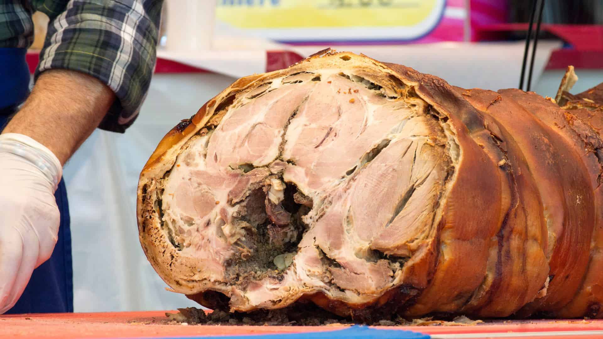 A large, roasted pork roll sliced open on a table, showing juicy meat and crispy brown skin.