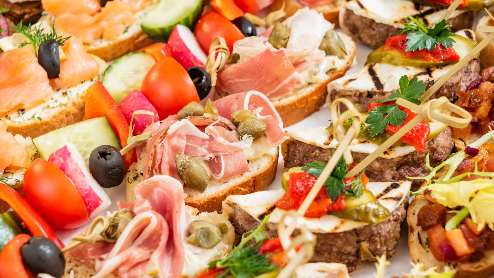 Assorted colorful canapés with meats, vegetables, cheese, and herbs arranged on a platter.