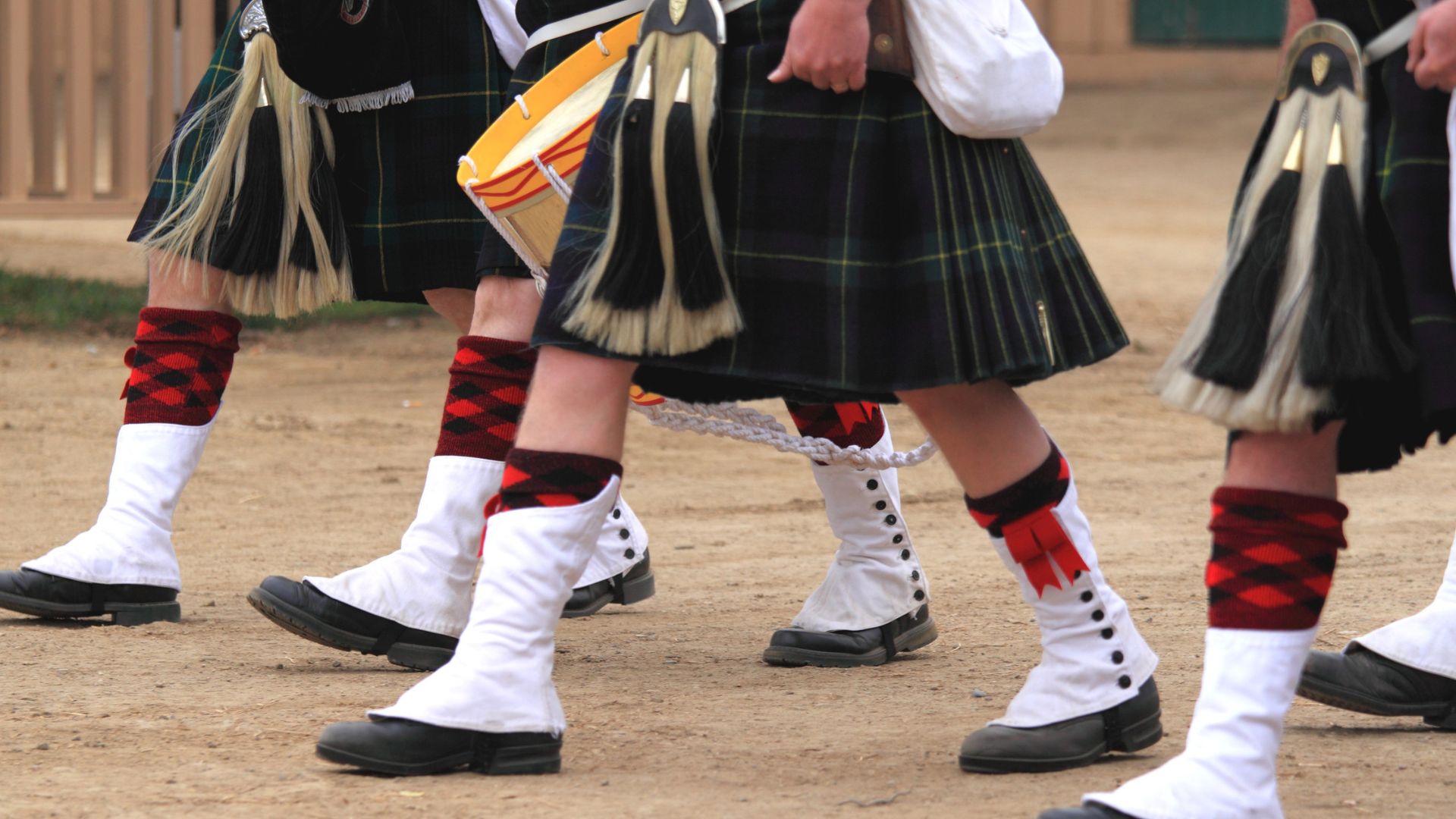 People wearing kilts, kilt hose, and sporrans, walking outdoors on a dirt path.