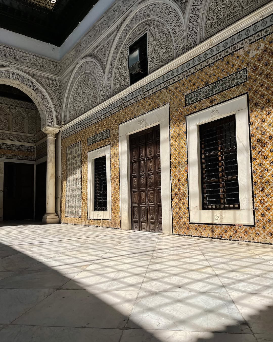 Sunlit courtyard with ornate arches, patterned tiles, and wooden doors casting lattice shadows on the floor—a perfect highlight for your Tunisia itinerary 1 day adventure.
