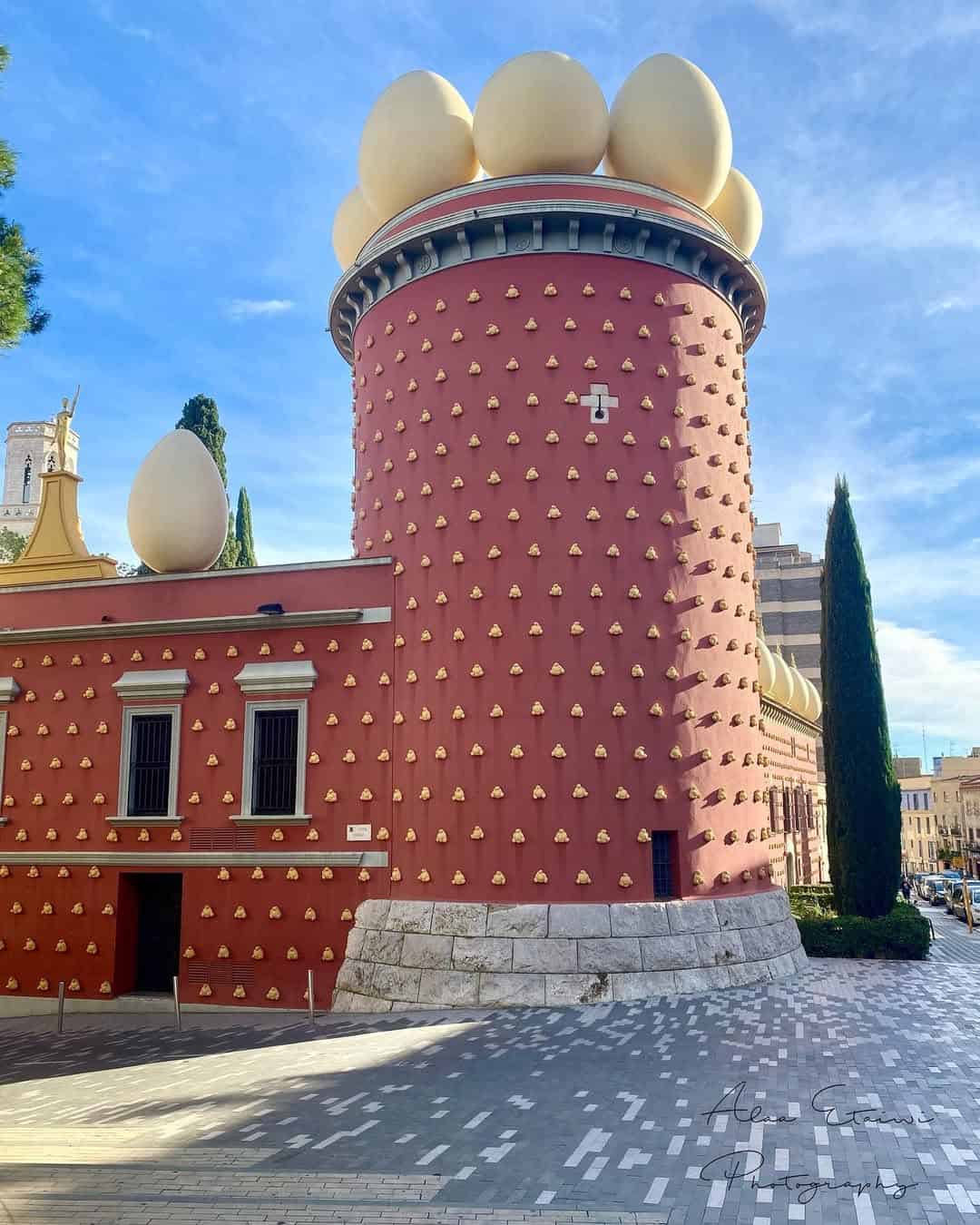 A pink building with golden accents, topped with large egg sculptures under a blue sky&mdash;a whimsical stop to include on your Barcelona itinerary.