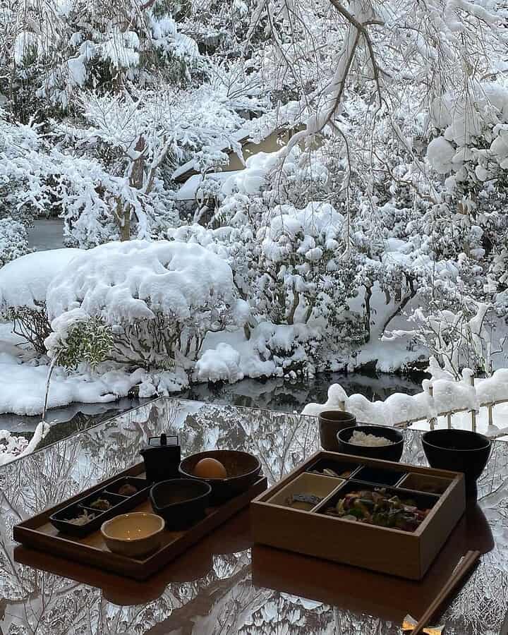 Two Japanese meal trays on a table with a snowy garden view in the background, offering the perfect setting for winter travel dining.