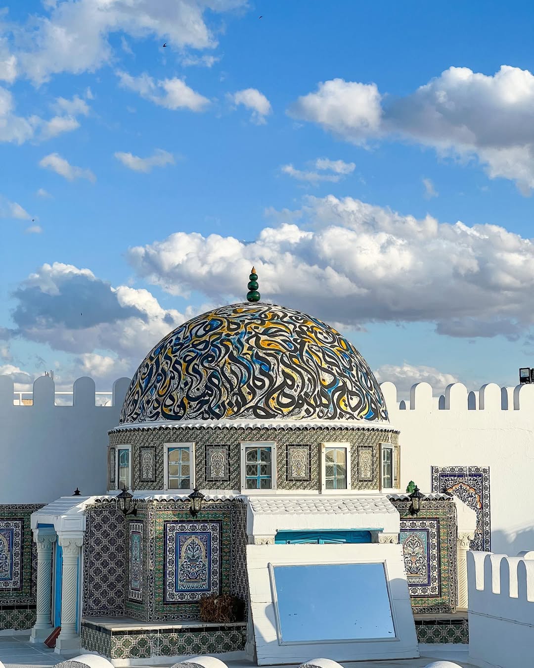 A colorful, patterned dome crowns a white building beneath a blue sky and drifting clouds—a perfect highlight for your Tunisia itinerary 1 day adventure.