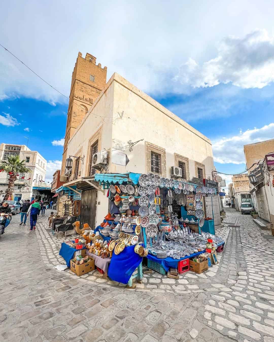 Street market stall selling plates and souvenirs in front of a tall building on a cobblestone street—a vibrant stop on any tunisia itinerary 1 day adventure.