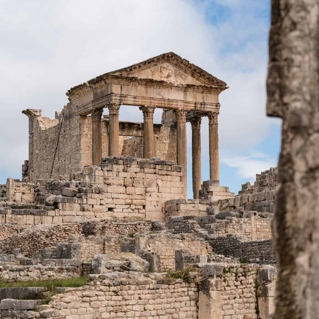 Ancient stone temple ruins with tall columns and steps under a partly cloudy sky—an unforgettable highlight to include in your Tunisia itinerary 1 day adventure.