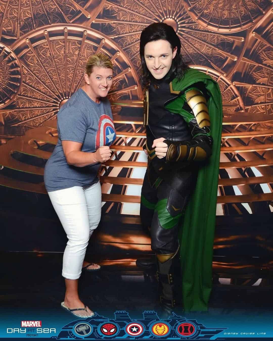 A woman poses playfully with a Loki cosplayer against a Marvel-themed backdrop at a themed cruises event.
