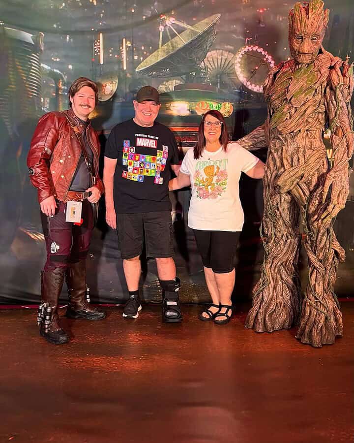 Three people and someone in a Groot costume pose in front of a colorful sci-fi themed backdrop, capturing the fun of themed cruises.