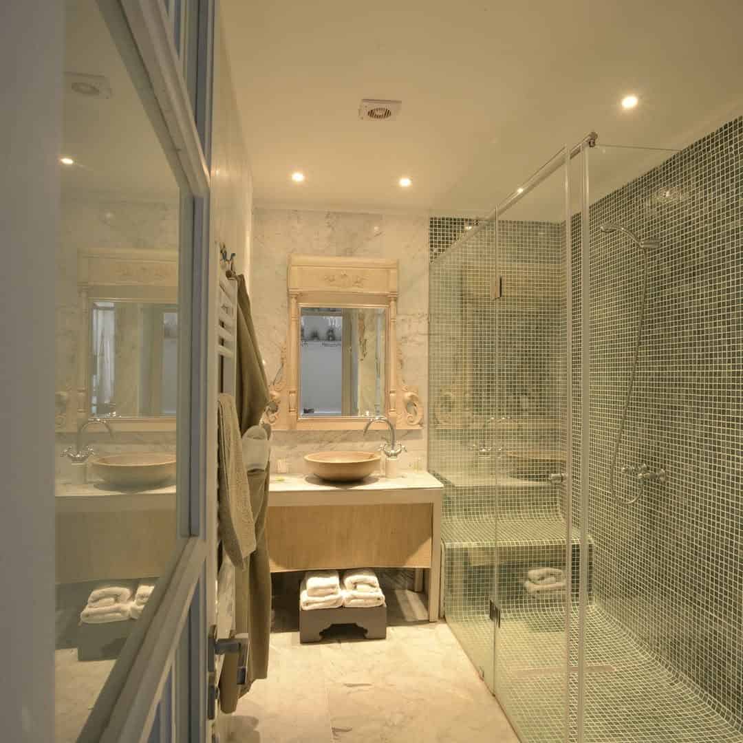 Modern bathroom with a glass shower, dual sinks, mirrors, and towels hanging on the wall—perfect for refreshing after your tunisia itinerary 1 day adventure.