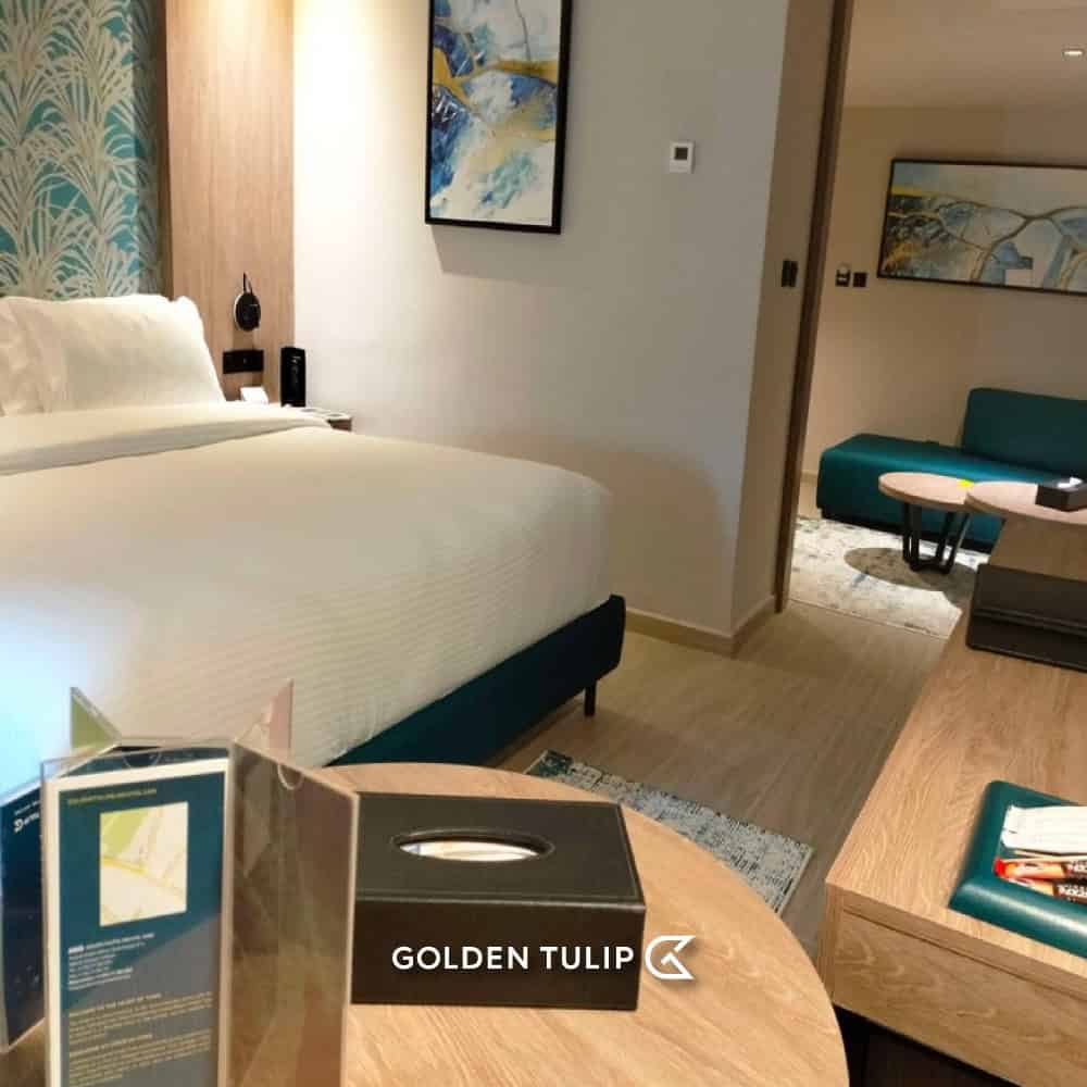 Hotel room with a large bed, modern decor, a sitting area—perfect for relaxing after completing your Tunisia itinerary 1 day adventure. "Golden Tulip" logo at the bottom center.