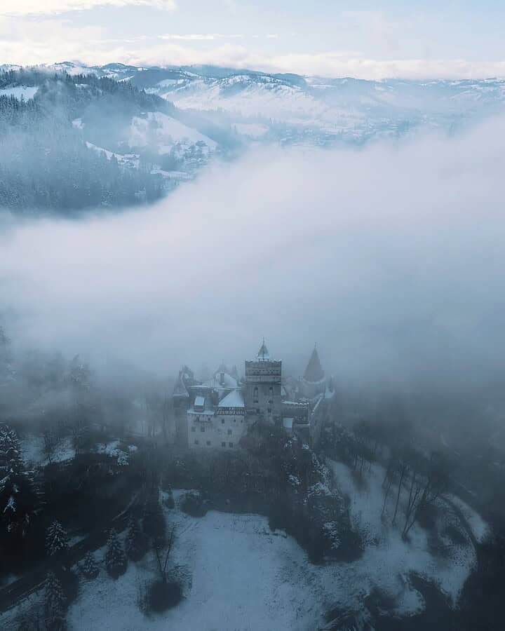 A castle surrounded by snow and misty fog, with mountains in the background&mdash;an enchanting scene perfect for winter travel.