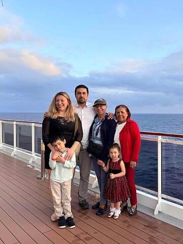 A family of six poses on a cruise ship deck during one of the popular themed cruises, with the ocean and a cloudy sky creating a stunning backdrop.
