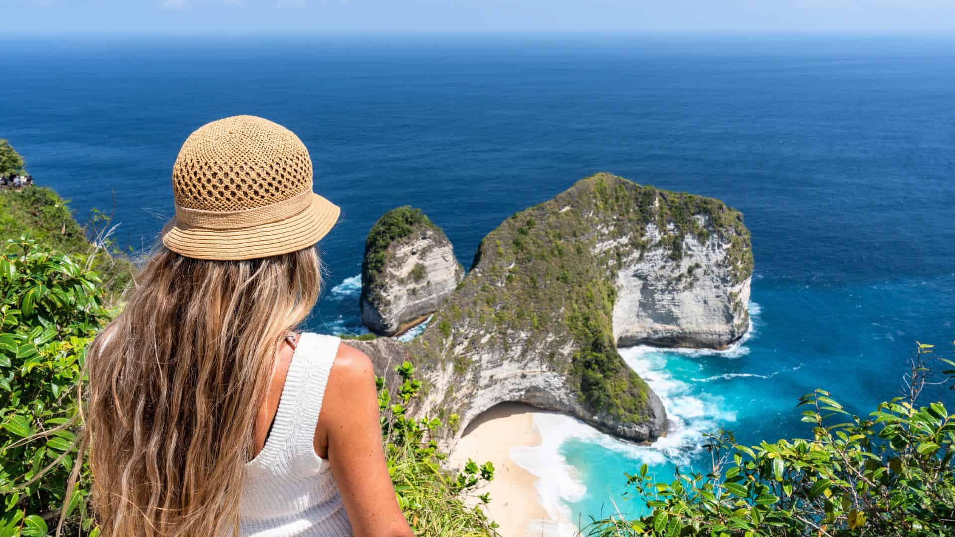 Woman in a sunhat overlooking cliffs and turquoise ocean at a scenic beach viewpoint.