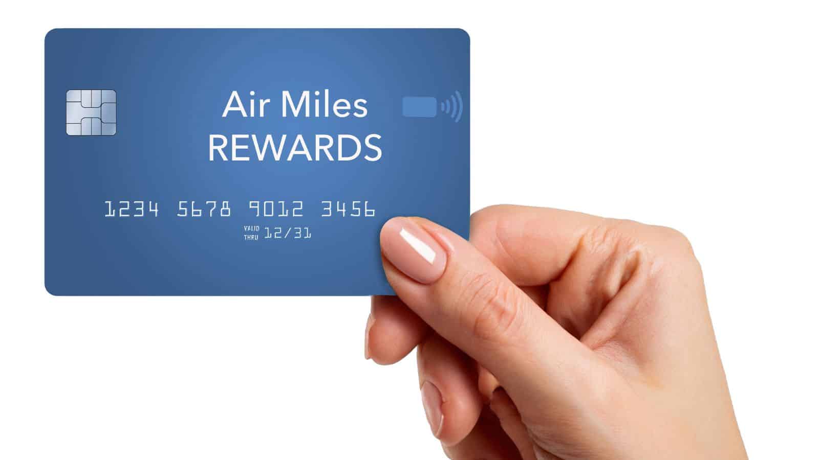 Hand holding a blue Air Miles Rewards card with numbers and a chip, on a white background.