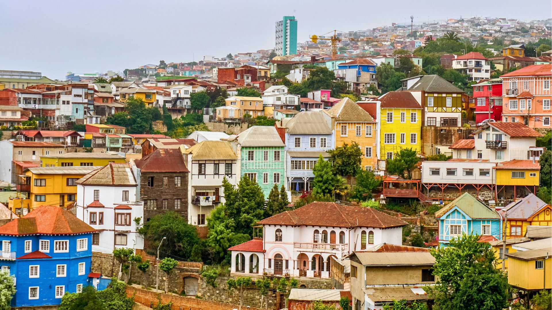 Colorful hillside houses densely packed in a vibrant neighborhood with lush greenery and cloudy skies.