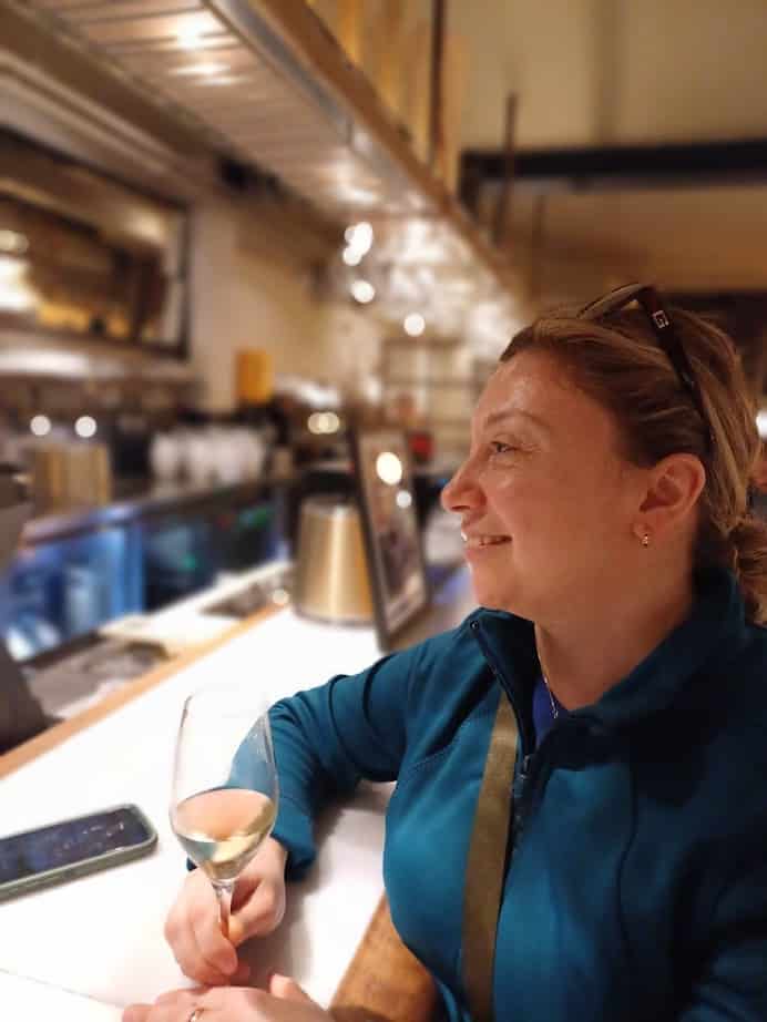 A woman smiles while holding a glass of white wine at a bar counter—an ideal way to unwind after exploring the best things to do in Barcelona.