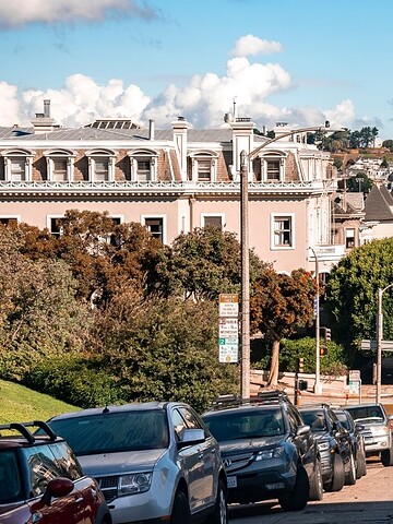A steep San Francisco street lined with parked cars and historic buildings, with a tower visible in the distance.