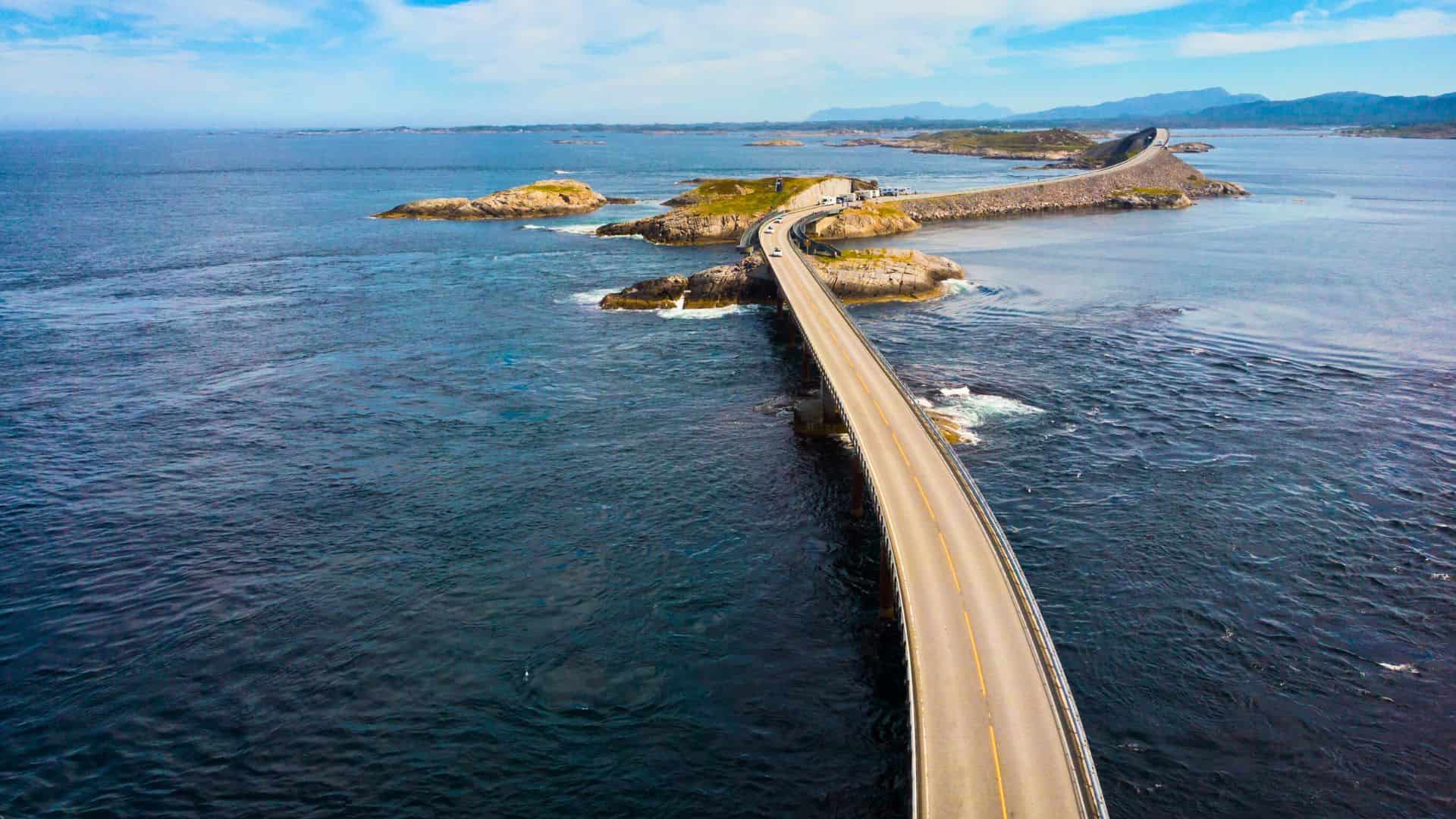 A winding coastal road crosses small islands over blue ocean under a partly cloudy sky.