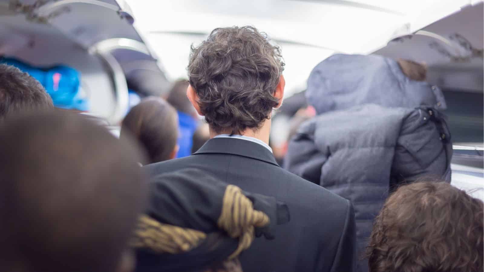 A man in a suit stands among passengers in a crowded train or subway, viewed from behind.