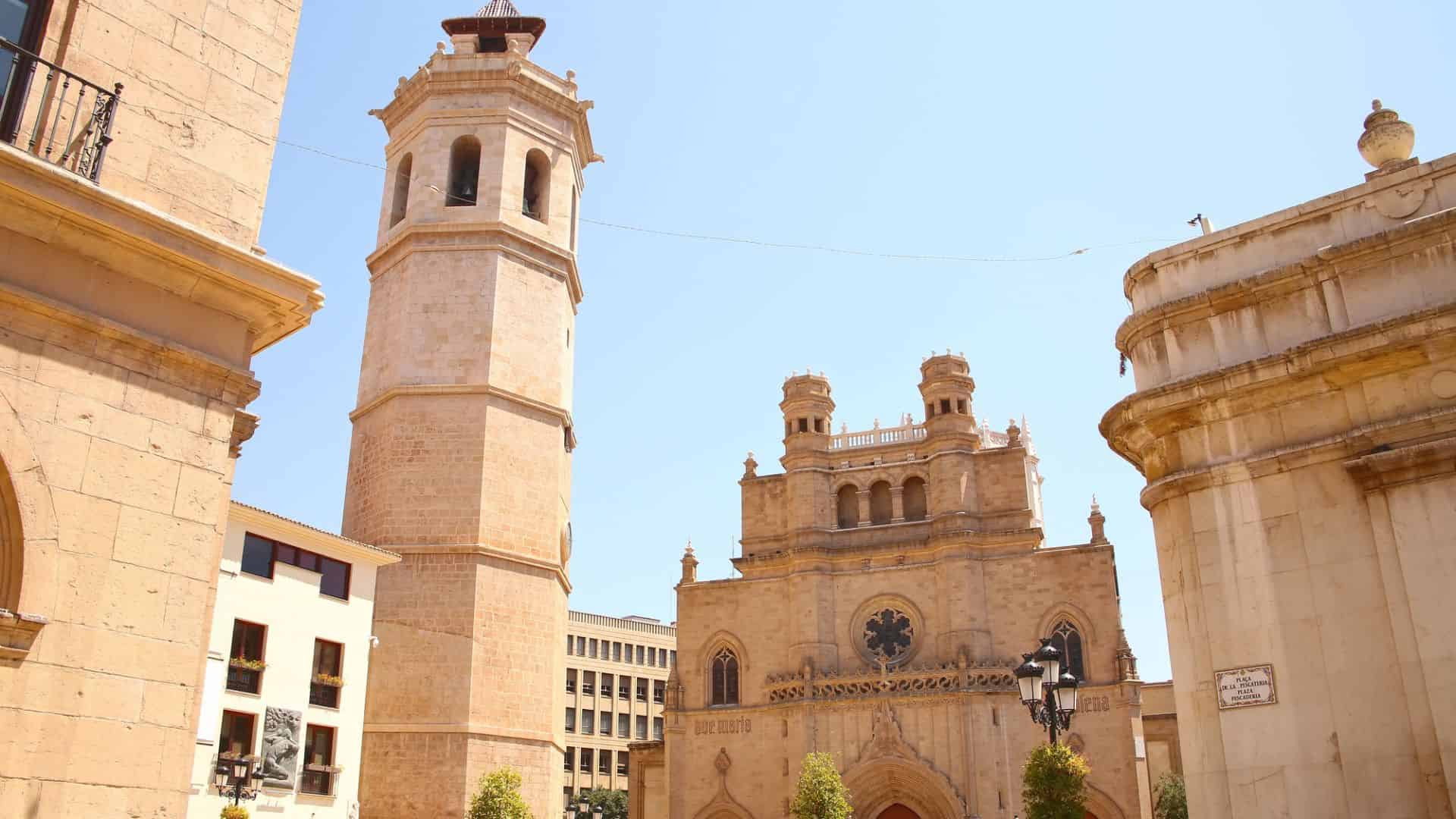 Historic stone church with twin towers and a tall bell tower under a clear blue sky.