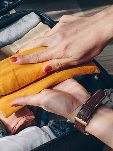 Hands packing a suitcase with neatly rolled colorful clothes, ready to explore new countries and avoid common travel mistakes on vacation.