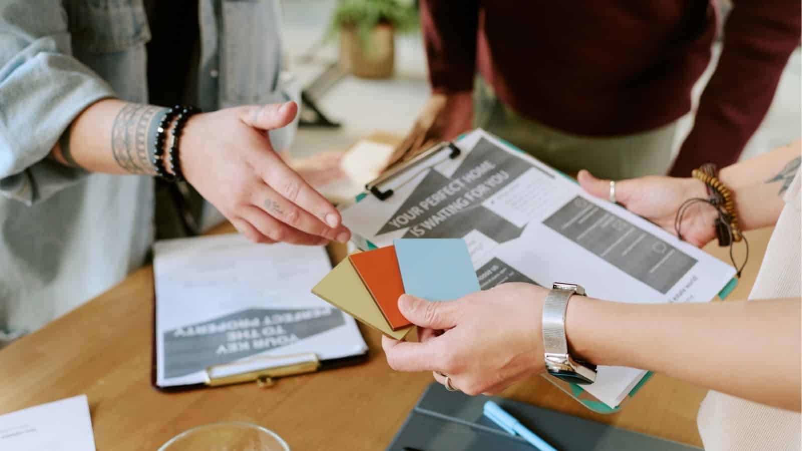 People discussing color swatches and documents at a table, planning a project or design.