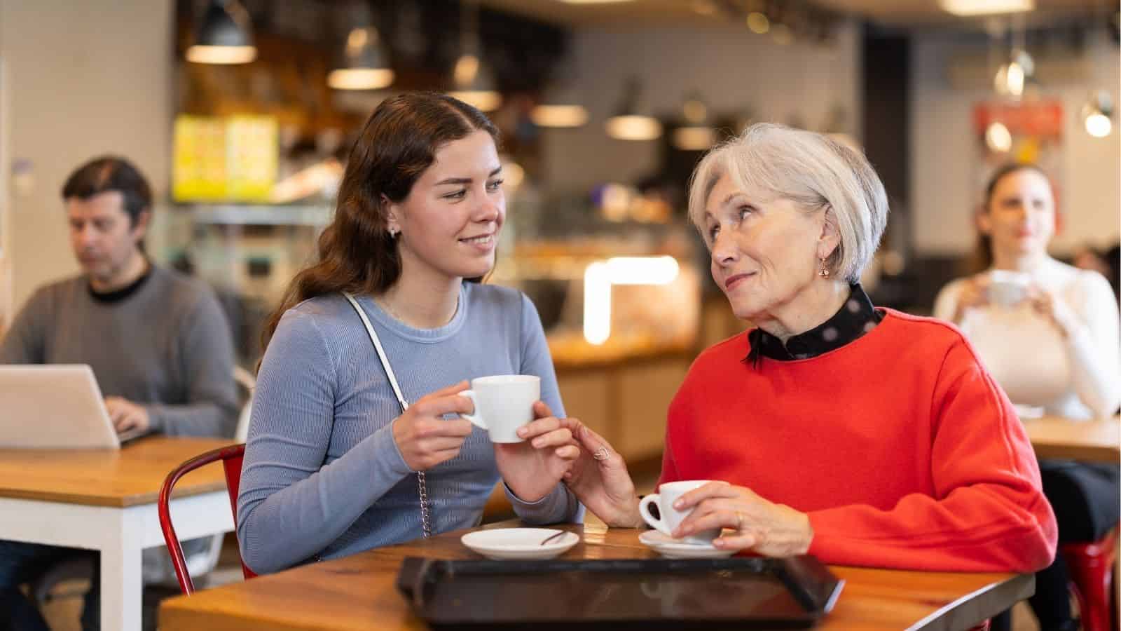 Young woman and older woman smiling and talking over coffee at a cozy café table.