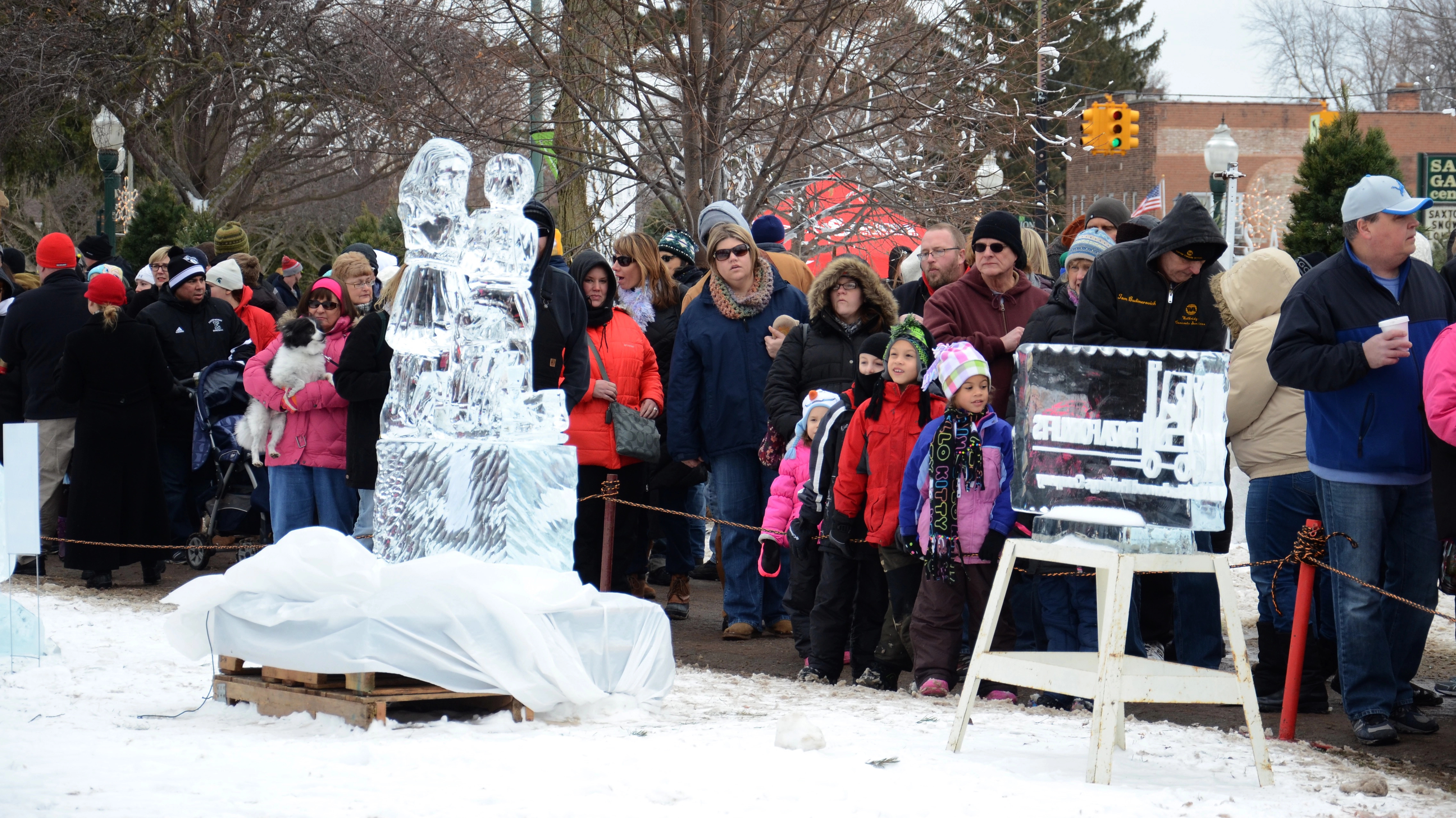 Crowd in winter clothes watches an outdoor ice sculpture event on a snowy day, celebrating one of the world&rsquo;s unique winter festivals.