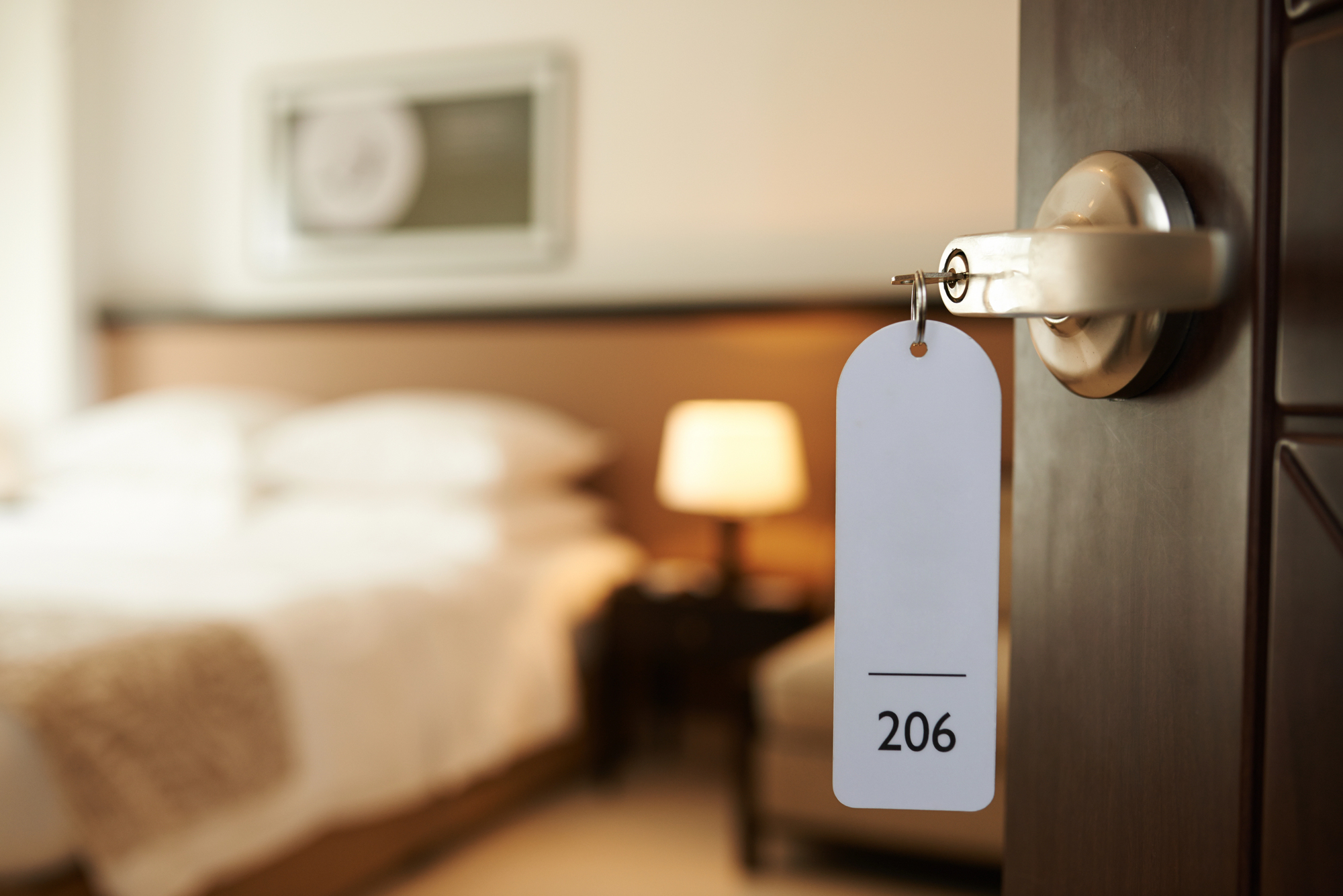 A hotel room door labeled 206 is open, revealing a bed, lamp, and blurred decor in the background, evoking the warm charm of Tuscany.