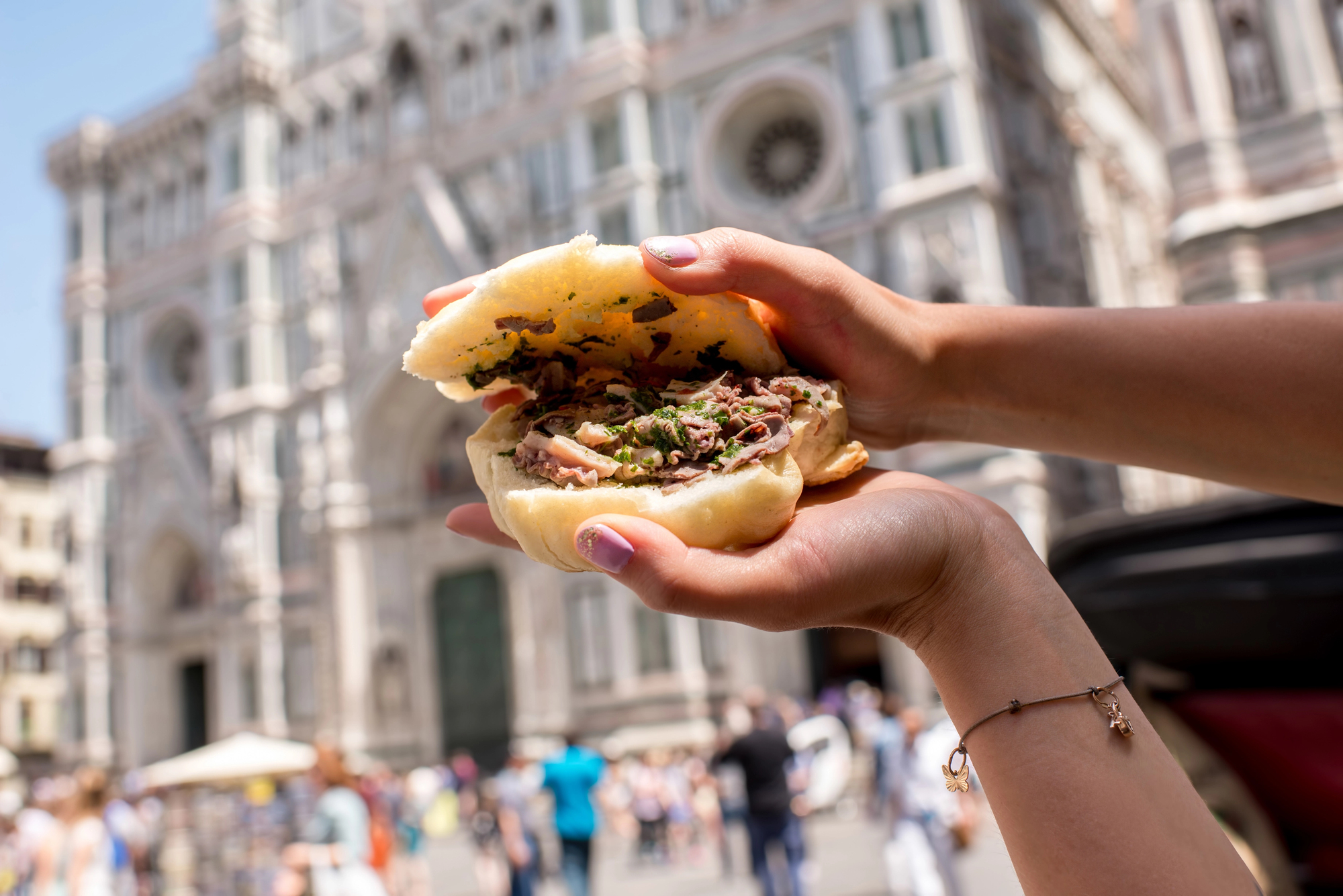 A person holds a sandwich filled with meat and herbs in front of a historic building with ornate architecture, capturing the essence of Florence food.