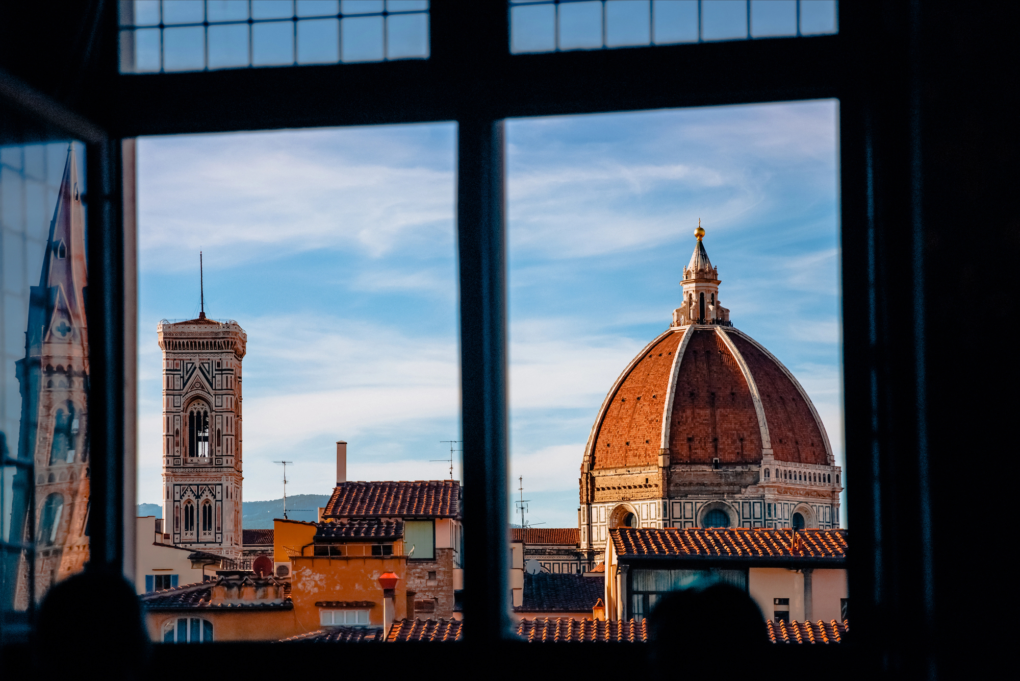 View through a window of Florence&rsquo;s Duomo and bell tower under a blue sky with scattered clouds&mdash;a must-see highlight on any Florence Italy itinerary.
