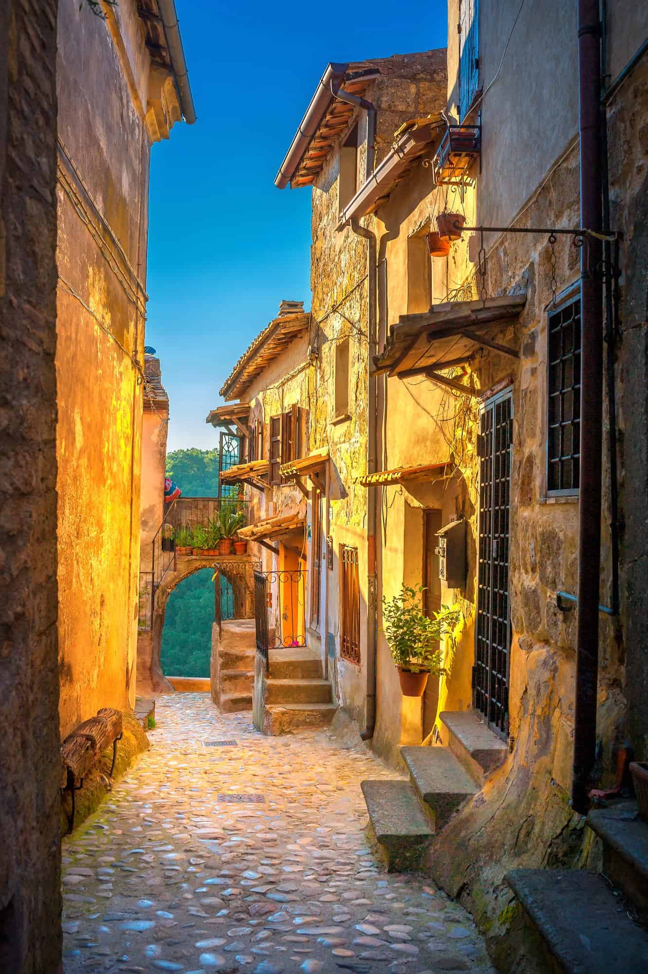 Narrow cobblestone street with warm sunlight on rustic buildings in a historic European village, capturing the charm found in any Tuscany travel guide.