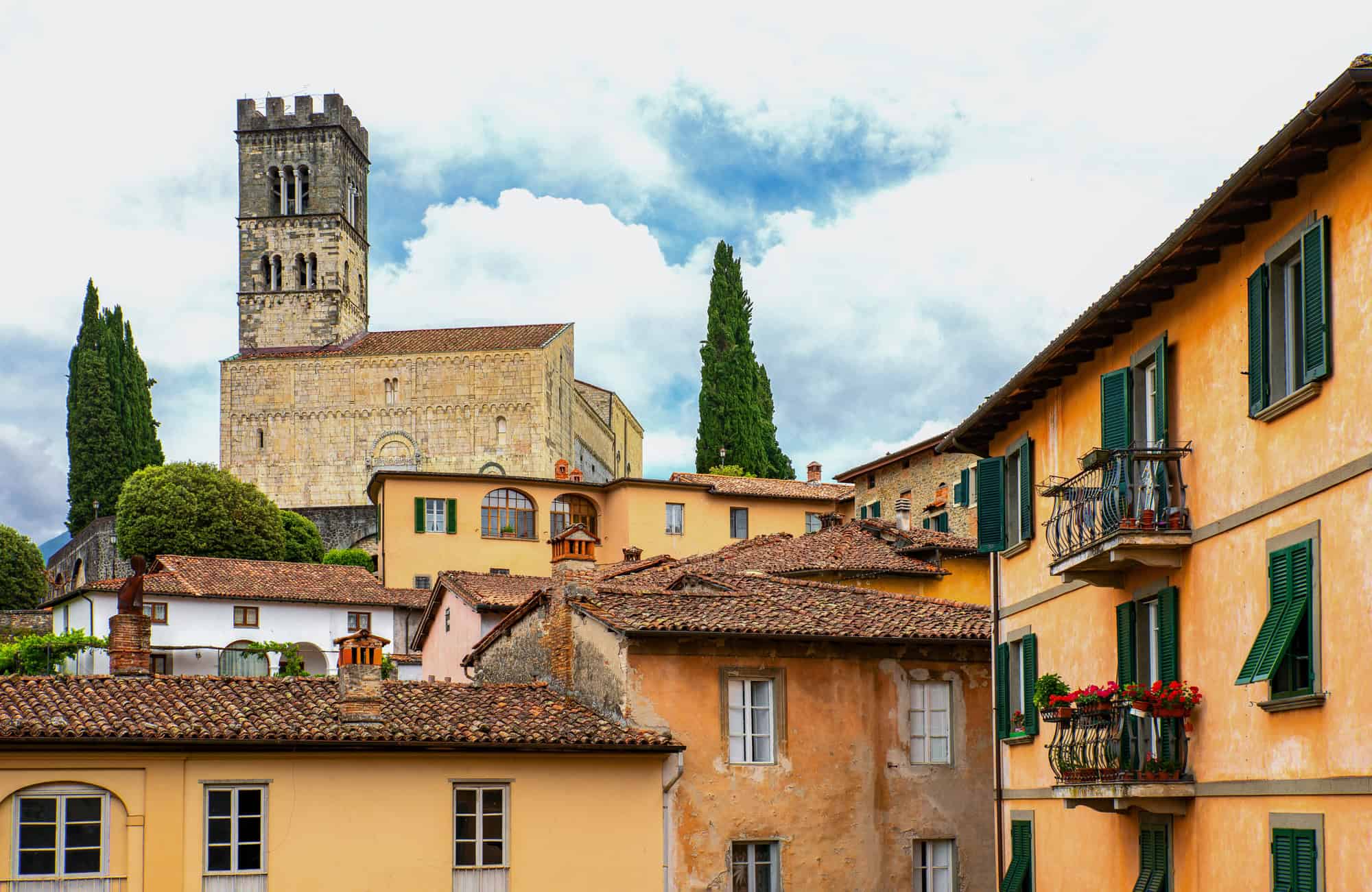Stone church tower and yellow houses with tile roofs in a charming Italian village, typical of Tuscany villages, under a partly cloudy sky.