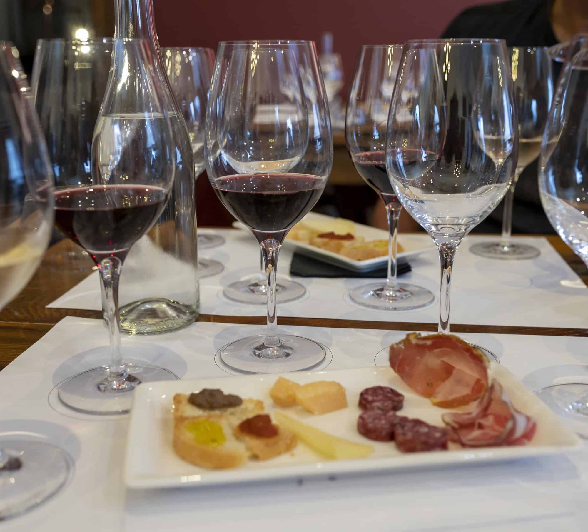 Wine glasses and a water bottle on a table with a charcuterie plate of meats and cheeses in the foreground, capturing the essence of Tuscany wine tours.