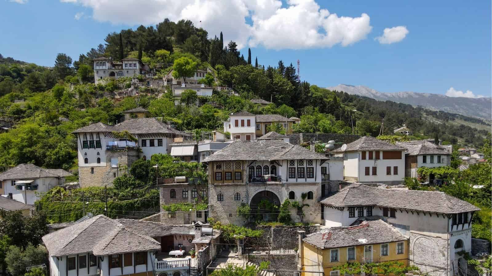 Stone houses with tiled roofs on a green hillside under a blue sky with clouds.