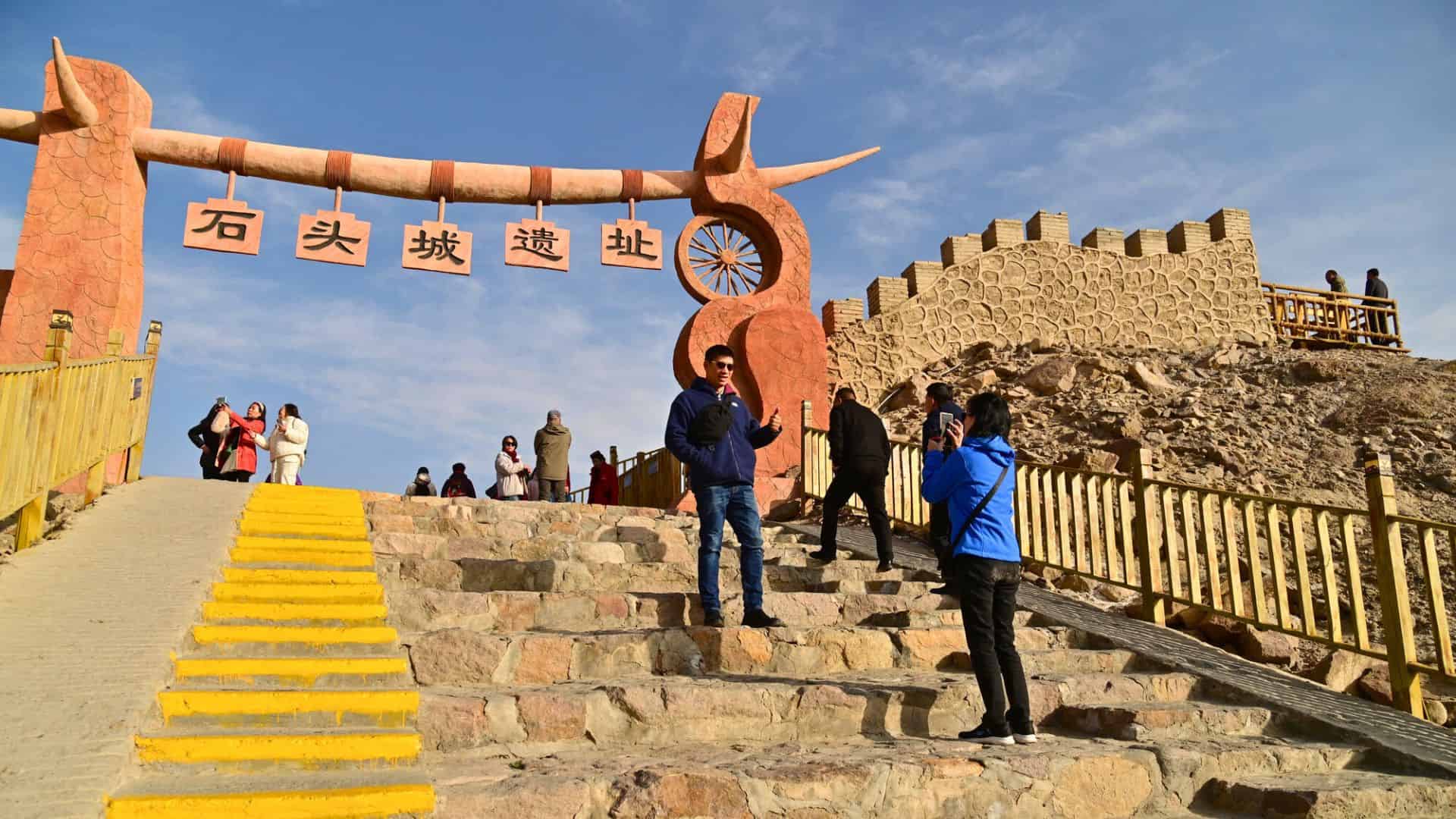 People pose for photos on stone steps at a historic site with a large gate and Chinese characters.