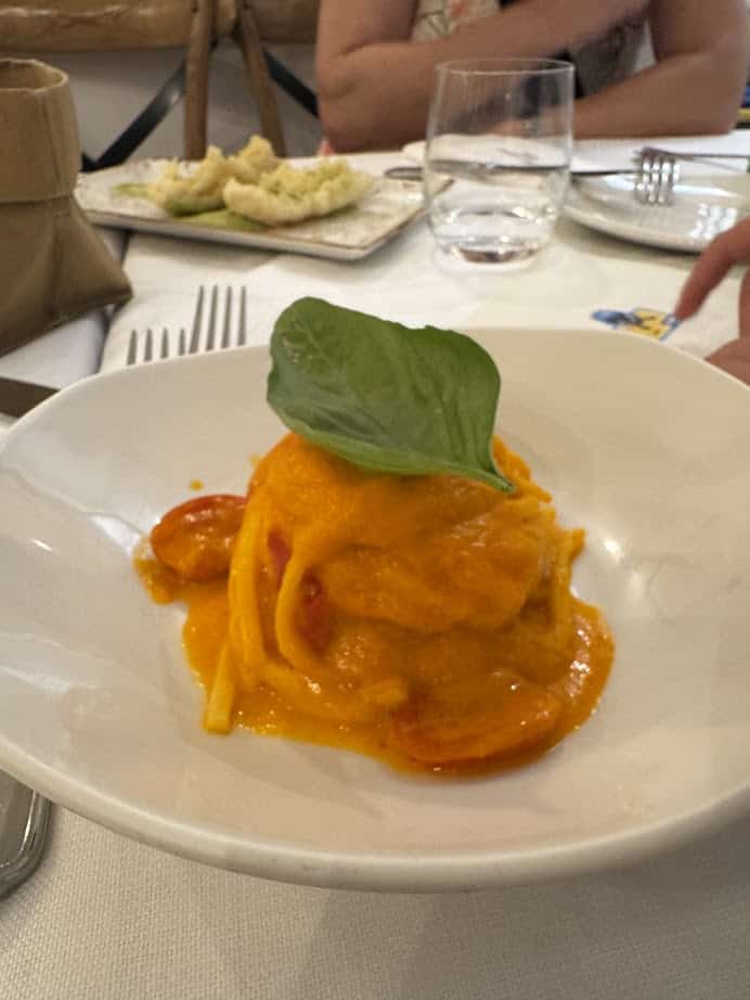 A plate of pasta with orange sauce, cherry tomatoes, and a basil leaf, set on a restaurant table—perfect for enjoying during your Rome with Kids adventure.