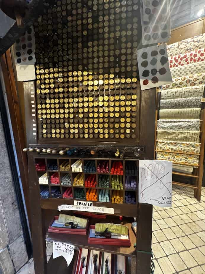 Shelf with colorful wax sticks, assorted seals, and a sign that says "FRAGILE PLEASE DO NOT TOUCH"—a charming find for any family itinerary while exploring Rome with kids.