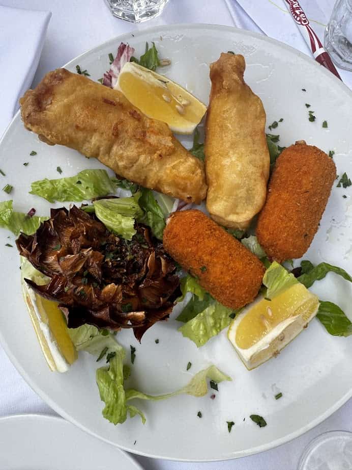 Plate of fried foods with lemon wedges, mixed greens, and a small serving of artichoke on a white tablecloth—a delicious taste of Rome with Kids that’s perfect for your next family itinerary.