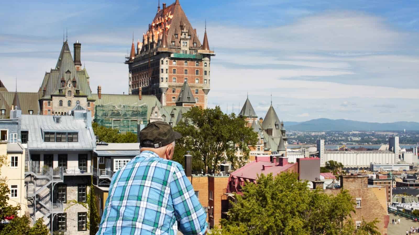An older man in a plaid shirt overlooks Château Frontenac and cityscape in Quebec City on a sunny day.