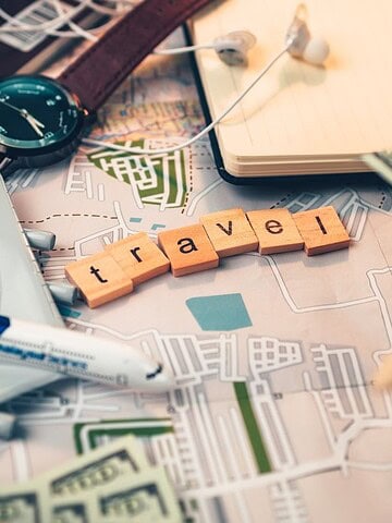 A map with a toy airplane, compass, money, and wooden blocks spelling "travel.