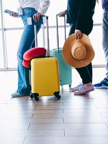 People standing in line at an airport with colorful suitcases, waiting with travel accessories.
