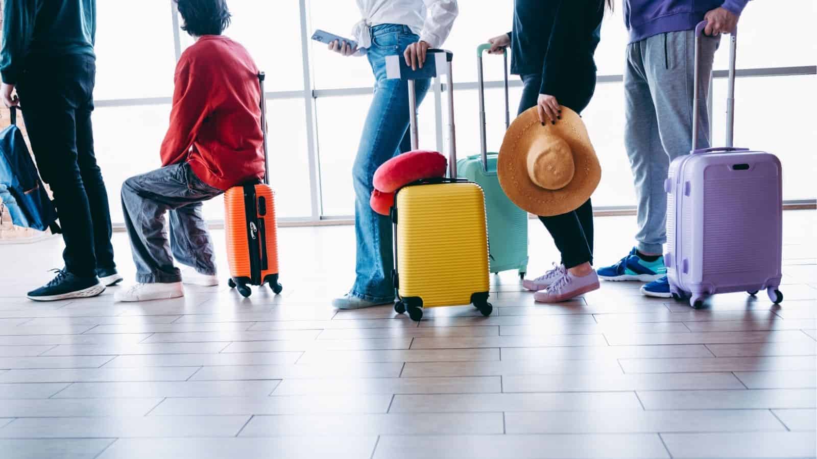 People standing in line at an airport with colorful suitcases, waiting with travel accessories.