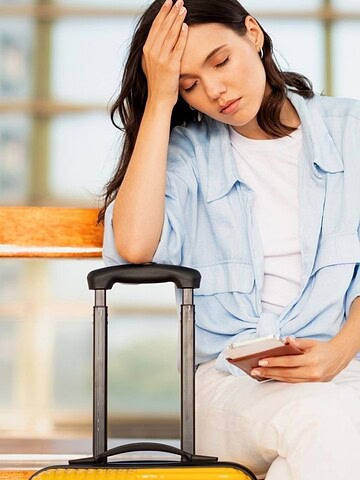 A woman sitting on a bench with her hand on her forehead.