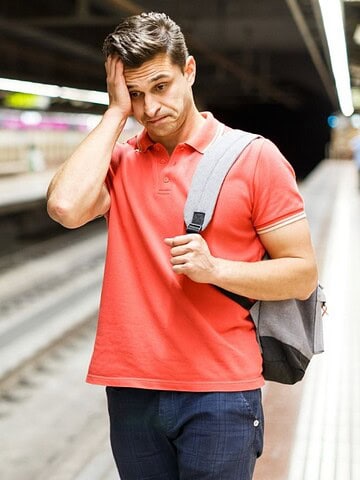 A man in a red shirt looks worried while waiting on an empty subway platform.