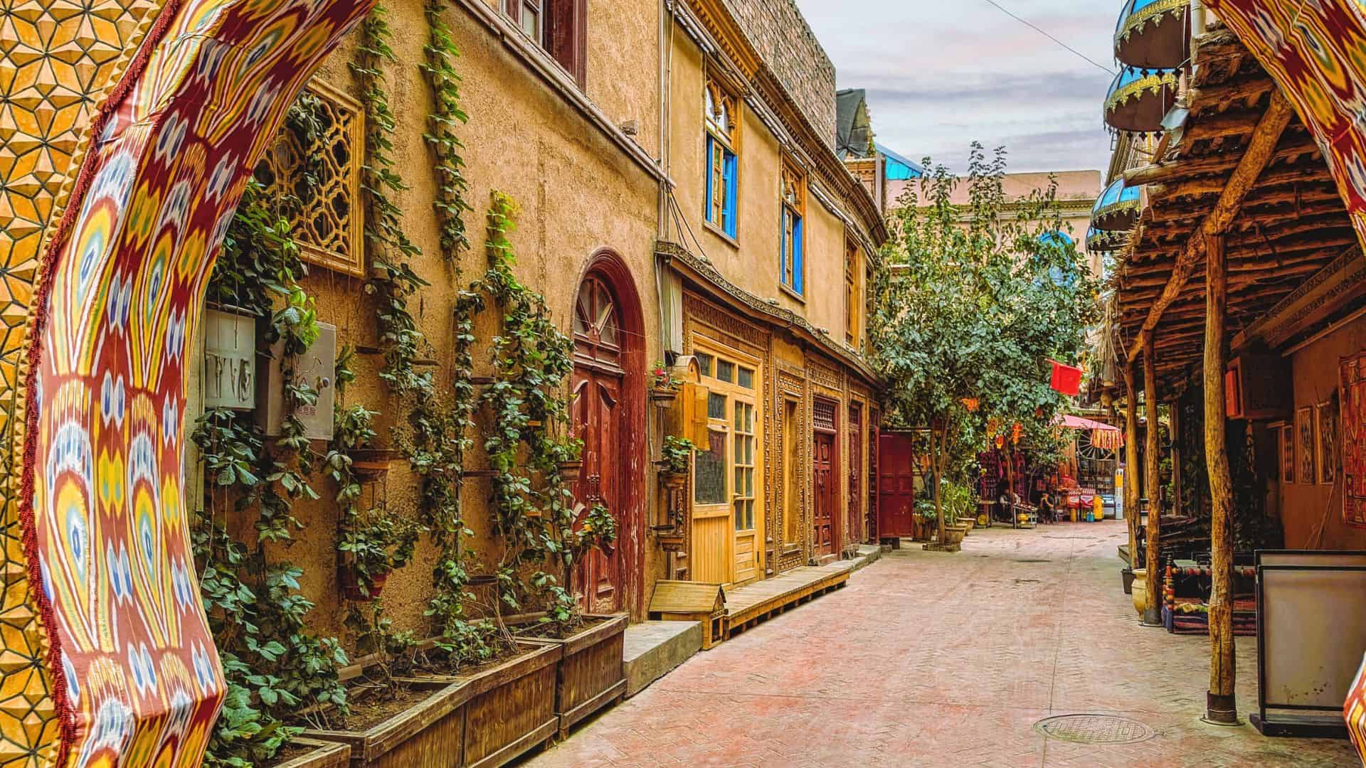 Colorful archway frames a narrow, vibrant alley with plants, wooden doors, and decorative details.