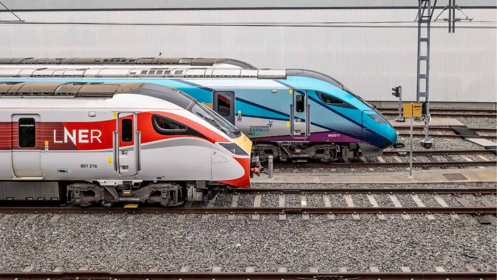 Two modern passenger trains, one red and white and one blue, are parked side by side on railway tracks.